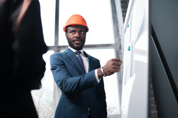 Photo from the back. Businesswoman and african american man reviewing house building plan