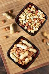 Roasted, raw peanuts and shelled in black ceramic bowls on a brown wooden table