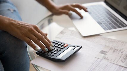 Crop wide banner view of woman sit at desk pay bills taxes on laptop online, manage home finances. Female busy calculating household expenses expenditures on calculator, make payment on computer.