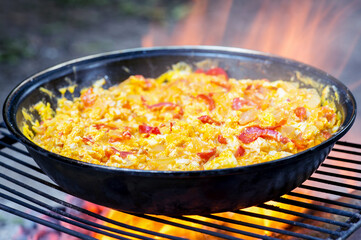 Omelet with vegetables in a frying pan on the grill close-up in the fiery flame of the fire. Selective focus. Background