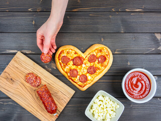 Heart shaped pizza on the table with woman's hand tasting the ingredient