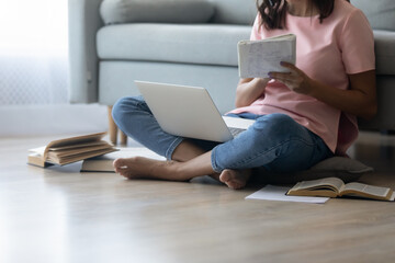 Fototapeta premium Crop close up of woman sit on floor at home make notes study online or work distant on computer gadget. Focused female student write in notebook take internet education course or training on laptop.