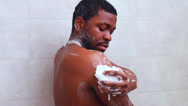 brazilian man washing body with shower sponge in white bathroom