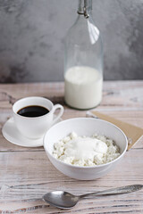 Cottage cheese with sour cream in a white bowl with coffee and milk on a white wooden table. Healthy breakfast. Rustic style.