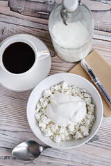 Cottage cheese with sour cream in a white bowl with coffee and milk on a white wooden table. Healthy breakfast. Rustic style.