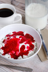 Cottage cheese with sour cream and raspberry jam in a white bowl with coffee and milk on a white wooden table. Healthy breakfast. Rustic style.