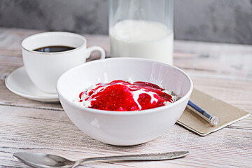Cottage cheese with sour cream and raspberry jam in a white bowl with coffee and milk on a white wooden table. Healthy breakfast. Rustic style.
