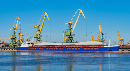Naklejka premium Cranes for loading on a ship top view. Tower cranes in the seaport. A cargo ship is waiting for loading of containers. Cargo barge at pier. Concept - cargo port services. Loading on a ship.