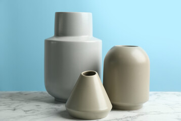 Stylish empty ceramic vases on white marble table against light blue background
