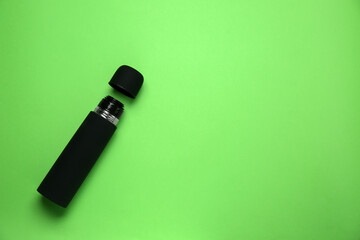 Black thermos and cup on green background, flat lay. Space for text
