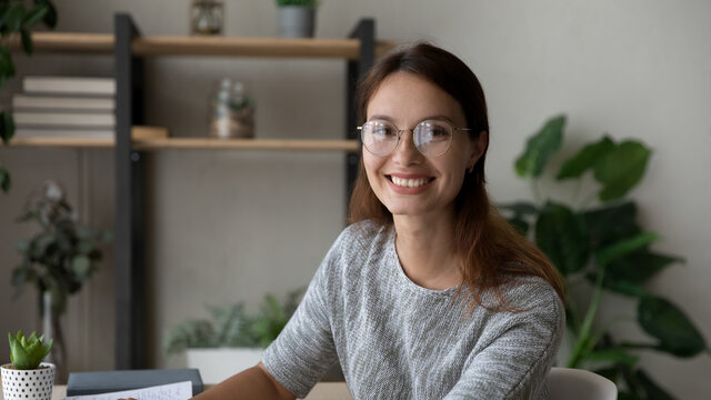 Wide banner view portrait of smiling millennial woman in glasses study at home office. Happy young Caucasian 20s female employee or student in spectacles look at camera posing in quality eyewear.
