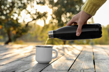 Woman pouring hot drink from thermos bottle into cup outdoors, closeup