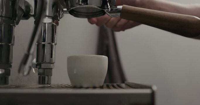 Slow motion low angle shot of espresso extraction from naked portafilter into white cup