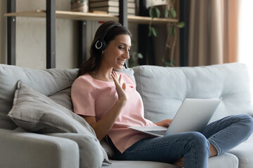 Smiling millennial indian Arabic woman in earphones wave greet talking on video call on laptop....