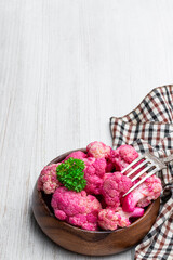 Pickled cauliflower with beetroot in wooden bowl on white wooden table