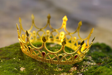 Beautiful golden crown on stone with green moss outdoors, closeup. Fantasy item