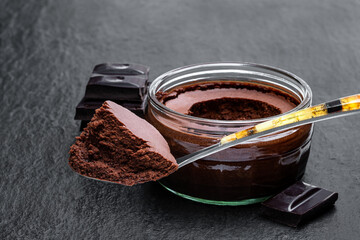 Dark chocolate mousse with ganache in glass jar on black stone background