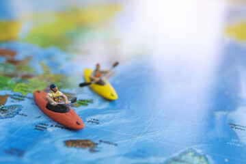 Fototapeta na wymiar Miniature people: Traveler sitting on board canoe and world map. Travel, vacation and summer concept.