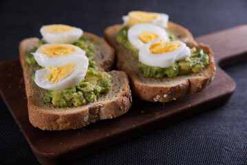 Sandwich prepared with oat toast, avocado and boiled egg, with dark backgrounds.