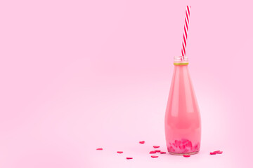 Small glass bottle with pink milkshake and red hearts copy space. Bottle with striped straws. A drink of love.