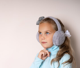 cute girl in fur headphones pensively looks up, resting her chin with her hand