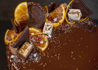 beautiful chocolate cake with oranges, poured with chocolate icing with drips on a dark gray background