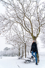 Chica joven en un parque nevado en un día de invierno con gorro de lana gris, jeans y cazadora negra