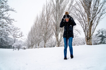 Chica joven en un parque nevado en un d&iacute;a de invierno con gorro de lana gris, jeans y cazadora negra