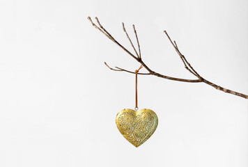 Gold patterned metal heart on a string hanging on a bare winter tree branch against a white background for valentine's day february 14