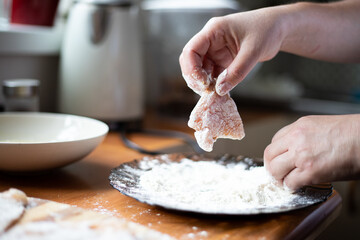 Breading chicken in flour. A person holding meat in his hand.