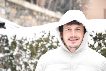 Portrait of smiling man next to snowy bushes. Dressed in a white jacket, brown hair with gray hair. Temporary Filomena.