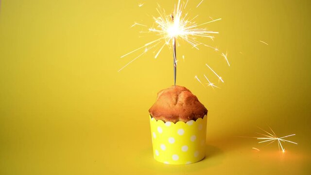 4k Homemade cupcake or muffin with sparklers in yellow decoration on yellow background, Celebration Valentine's day. Holiday, anniversary of married couple, birthday, monocrome	