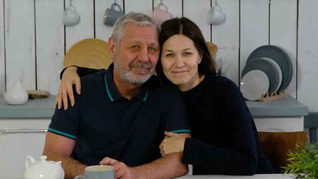 Elderly beared man and adult daughter at the kitchen smiling happily anf hugging, happy family