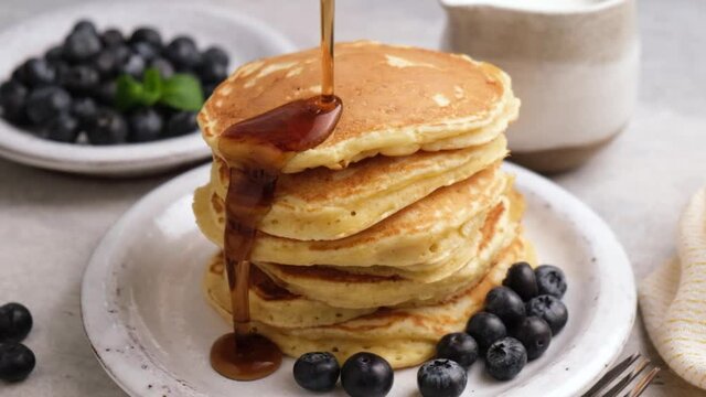 Maple syrup pouring over stack of pancakes in slow motion. Sweet breakfast food, pancakes with syrup and blueberries