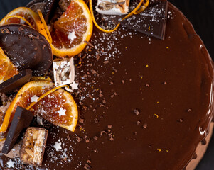 beautiful chocolate cake with oranges, poured with chocolate icing with drips on a dark gray background
