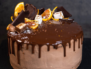 beautiful chocolate cake with oranges, poured with chocolate icing with drips on a dark gray background