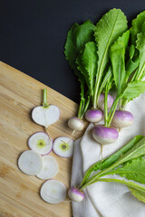 slice of fresh violet and white radish with entire radish on wood cutting board and white towel on black background. space for text on the right. top view.