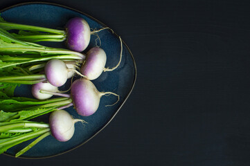 bunch of fresh radish in a blue plate on black background with space for the text on the right. top view