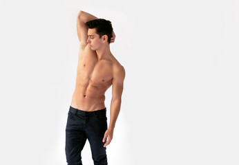 Fototapeta premium Sexy young man with nacked torso in black jeans, posing in studio with his hand raised, isolated on a white background.
