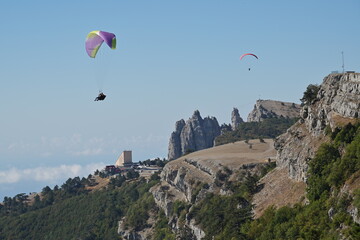 Two paragliders flying over cliffs in the mountains at summer.