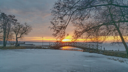 Sunrise in a cold winter morning with a view of icy lake bridge and trees