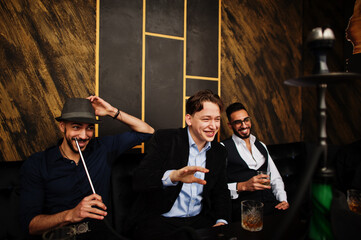 Fototapeta na wymiar Group of handsome retro well-dressed man gangsters spend time at club, smoking hookah. Multiethnic male bachelor mafia party in restaurant.