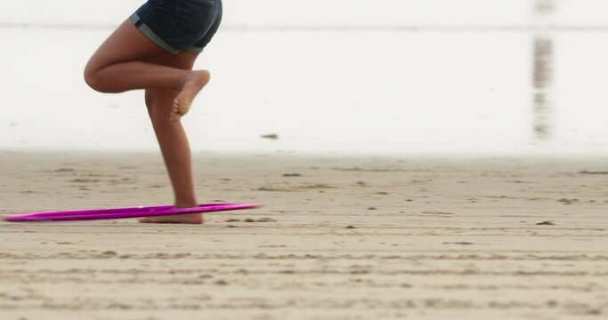 Woman twirling hula hoop using one leg on a sandy beach. Girl doing fitness activity by the sea. High quality 4k footage