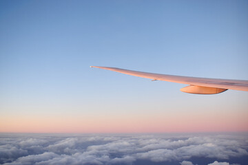 Fototapeta premium Aircraft wing above cloudscraper with horizon of pink and blue sky,view from airplane window.