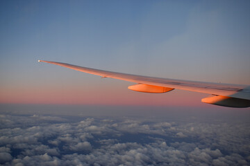 Fototapeta na wymiar Aircraft wing above cloudscraper with horizon of pink and blue sky,view from airplane window.