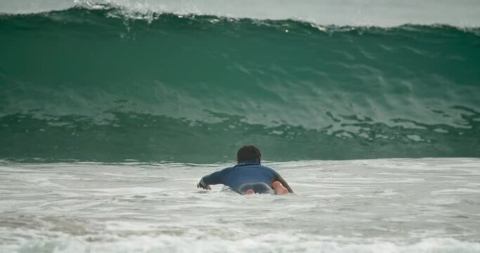 Wave rider laying onto the surfboard while swimming towards open water. Male surfer wears blue diving suit and uses yellow board. High quality 4k footage