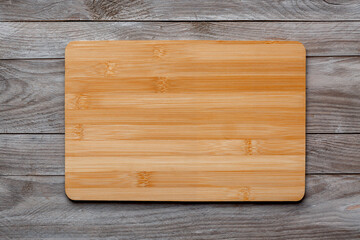 New rectangular wooden bamboo cutting board on wooden table background. Top view. Mock up for food project.