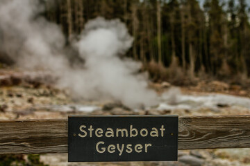 close up of focuse on steamboat geyser sign with blurry gayser on background in yellowstone national park in america
