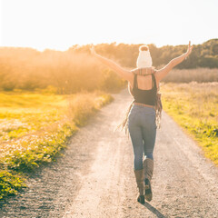 Fototapeta premium girl walking down a dirt road at sunset with open arms. She is on her back and the light is golden.