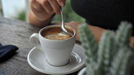 European girl sits at a table in a public place with a cup of coffee on a wooden table